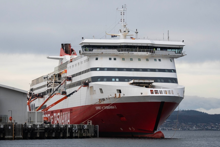 A large white and yellow cruise ship sits in the waterfront of a city.