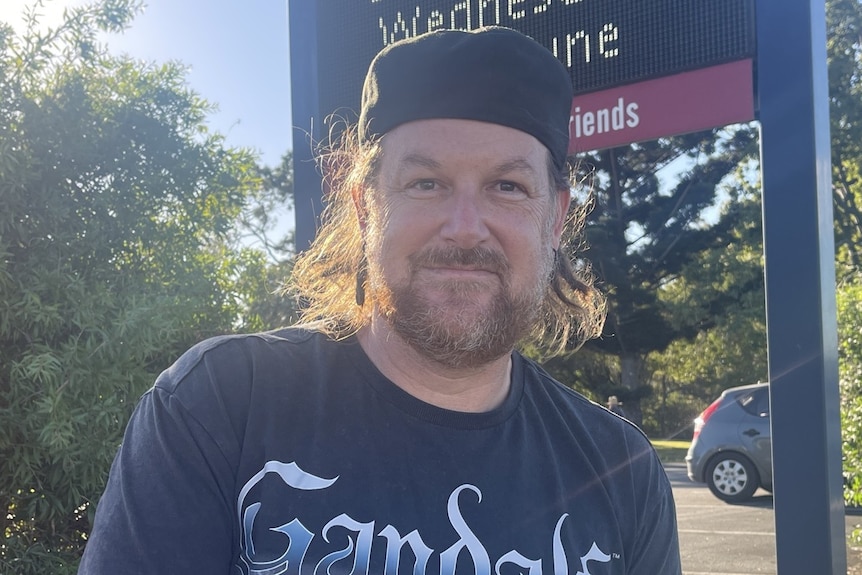 A man in a backwards cap smiling with a sign in the background