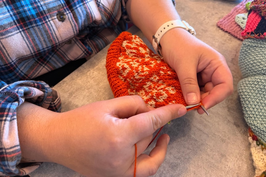 Two hands hold knitting needles working with red yarn.