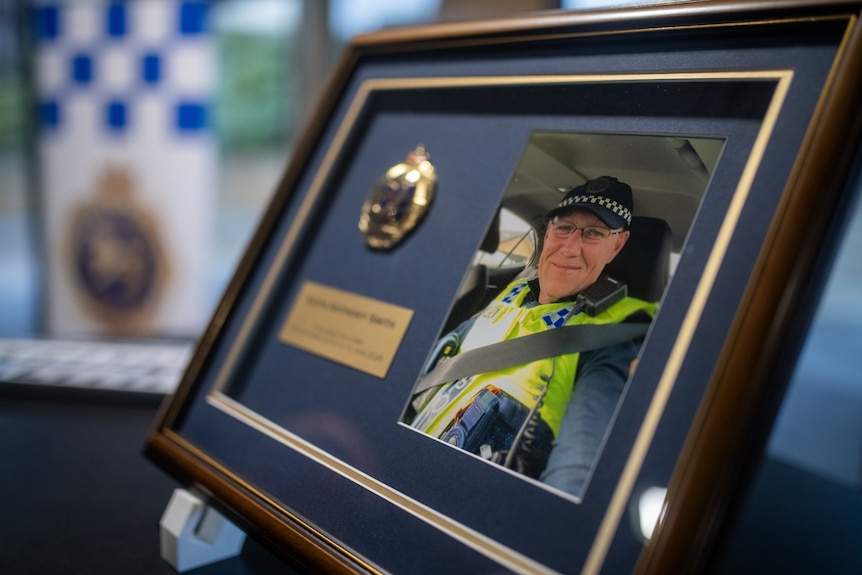 A commemorative plaque showing a photo of Keith Smith as well as his police badge, sitting on a table.