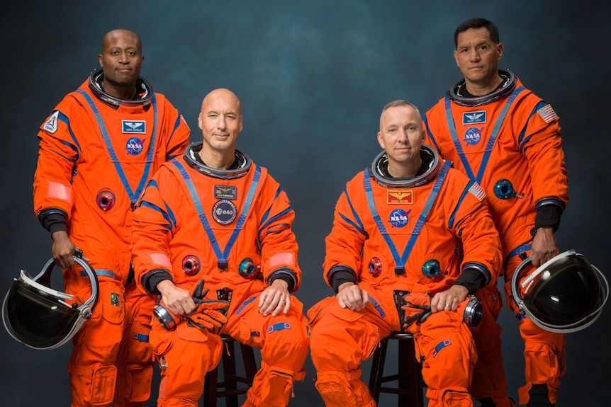 Four male astronauts in orange spacesuits, posing for an official portrait.