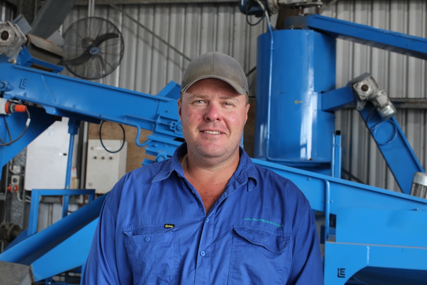 A farmer smiling for a photo in front of a macadamia sorter.