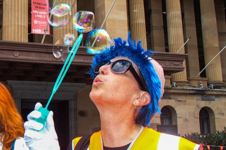 A person in orange hi-vis blows bubbles.