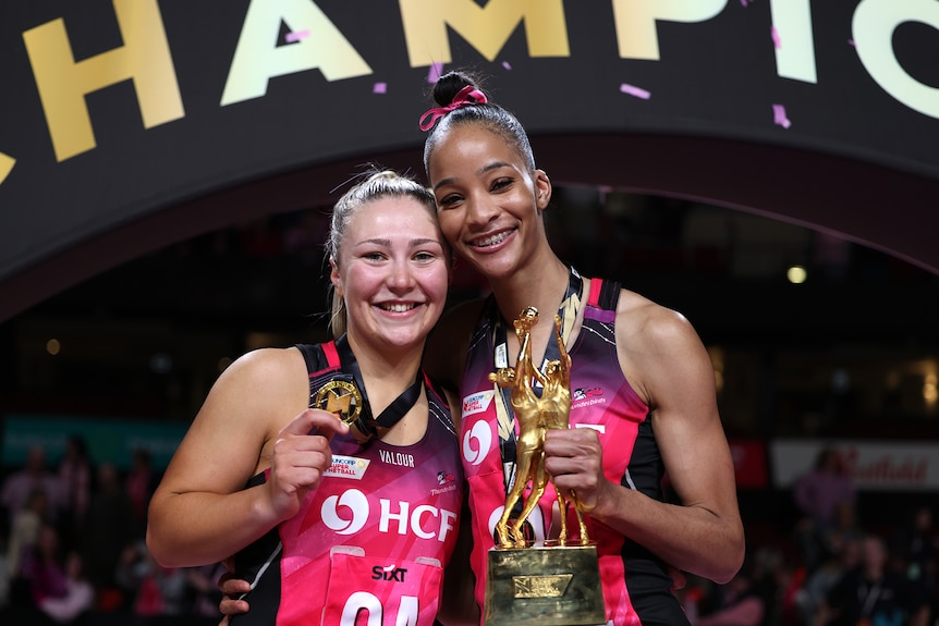 Two netball players hold medals
