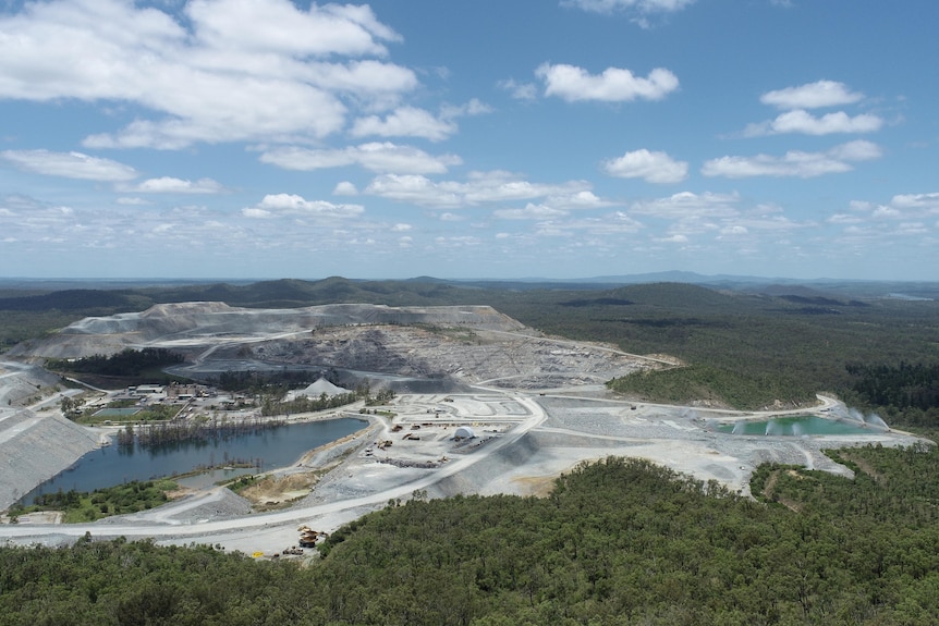 A wide aerial view of bushland with a large mine site in the middle with water in basins