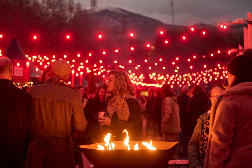 People stand around an open fire at night.