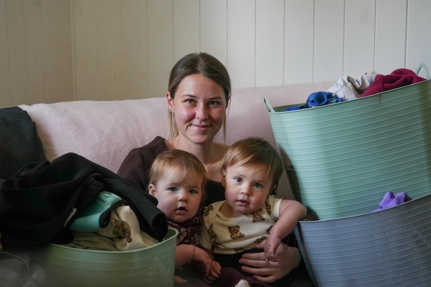 young woman with two toddlers on her lap, surrounded with baskets of laundry