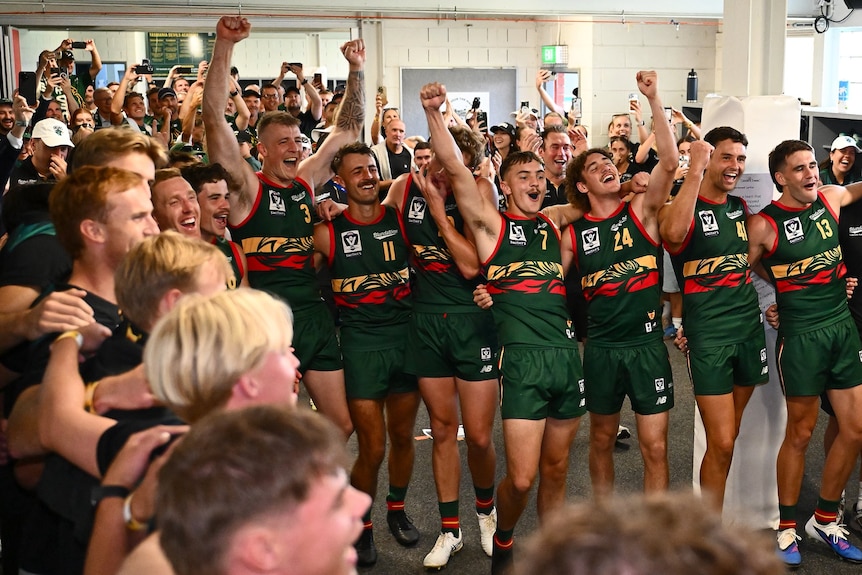Australian Rules football team and supporters rejoicing in a clubroom.