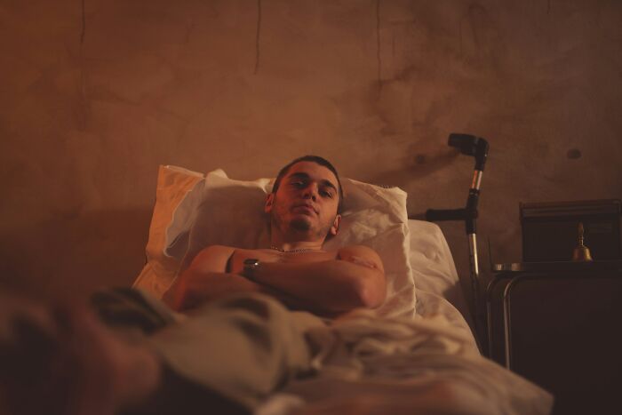A young man with visible scars on his arm lies in a hospital bed. Nurses often face unexplainable patient events.