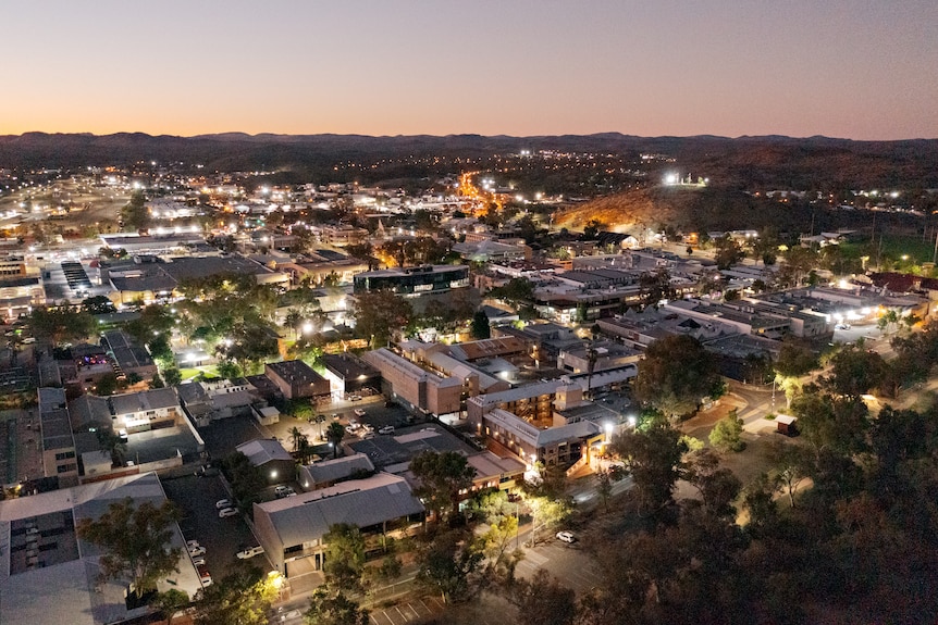 An aerial view of Alice Springs city centre at dusk, with the city well lit by street lights.