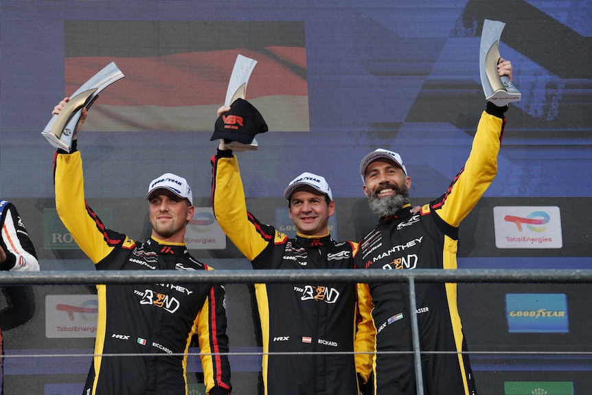 Three drivers holding up trophies on the podium after an endurance race