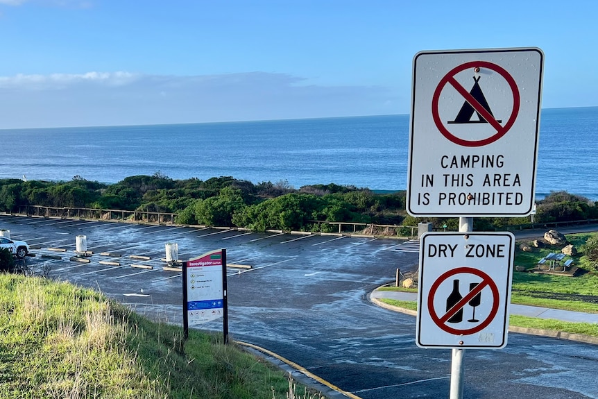 A no camping sign next to a carpark at a beach