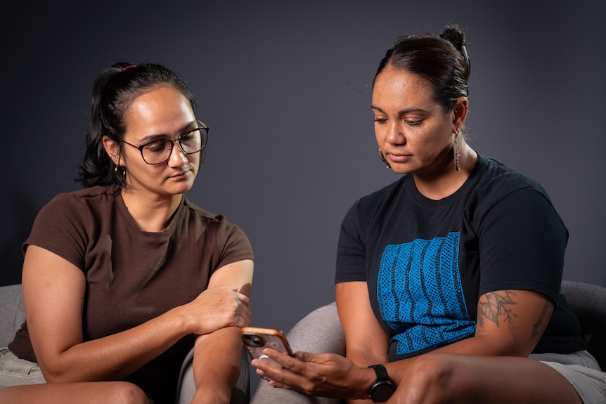 Two seated women look at a phone held by the woman on the right