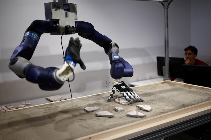 Human-like robot arms move broken pieces of mosaic tiles around inside a glass box