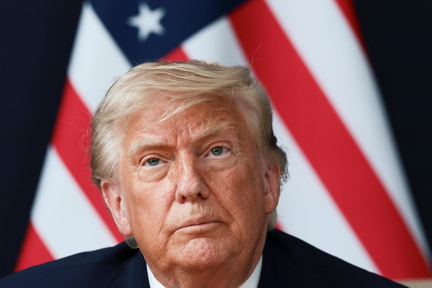 A close up of Donald Trump's face in front of an American flag.