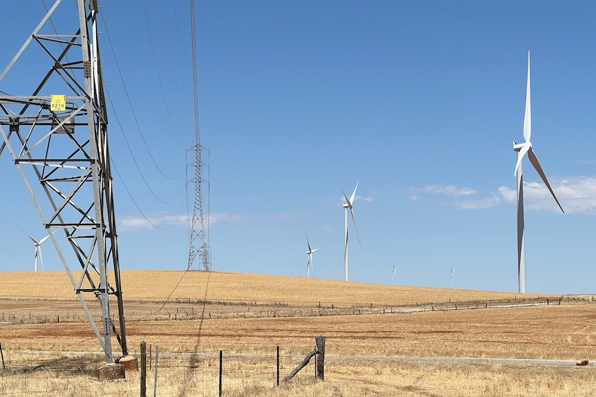 Transmission line towers and wind turbines in a dry country area.