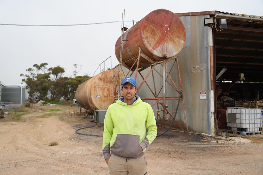 A man in hi-vis and a cap stands in front of two diesel tanks.
