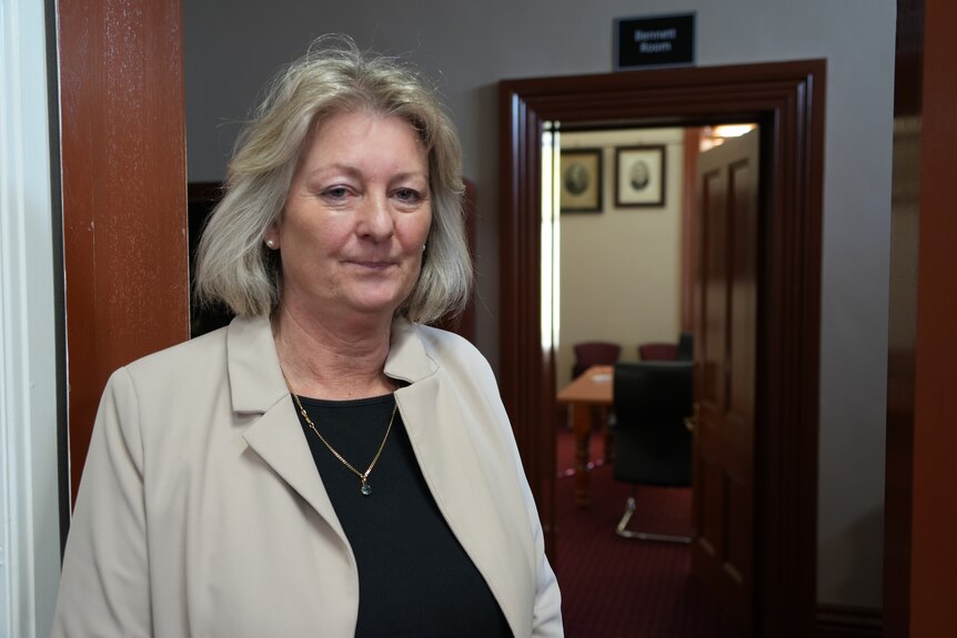 Middle aged woman with short blonde and grey bob looking serious inside council building.