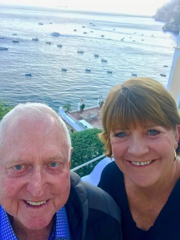 A man and a woman smiling into the camera in front of the ocean.