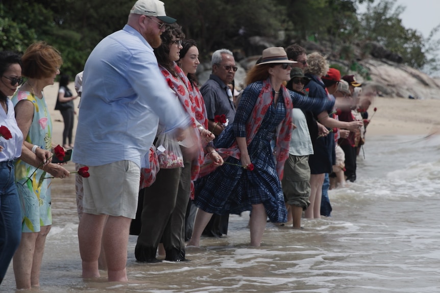 Line of people in shallows throw flowers into the sea