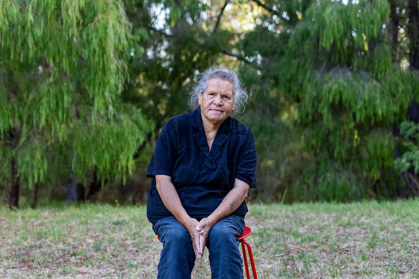 A woman sitting on a chair in front of bush.