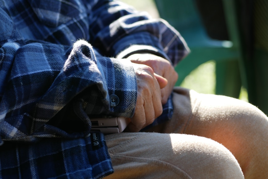 hands adorned in a blue flannelette shirt resting in a lap