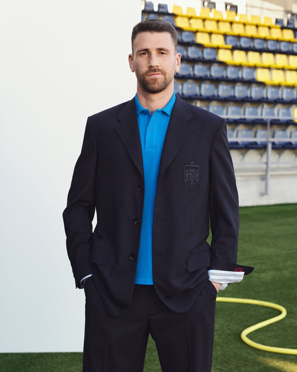 Person wearing a dark blazer and blue shirt, standing in front of stadium seats.