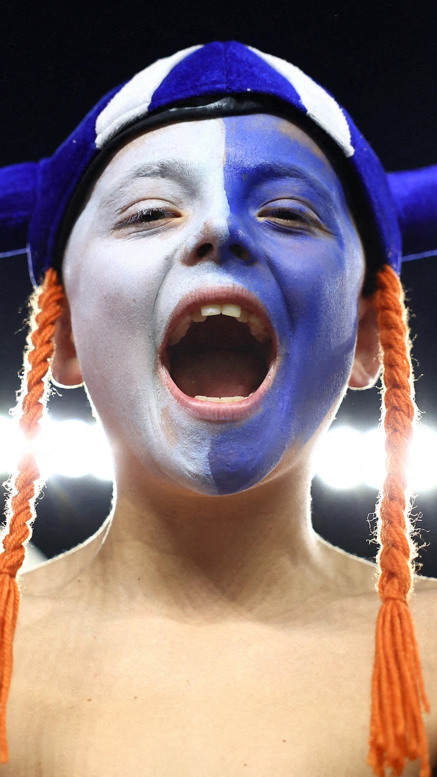 a boy wearing a horned helmet and white and blue face faint cheering