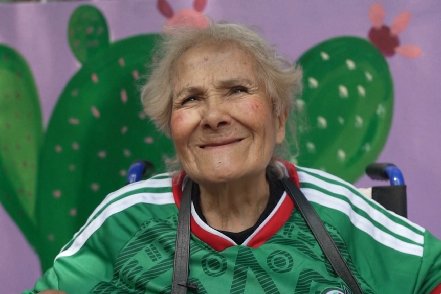 an older woman smiles at the camera waring a mexico jersey