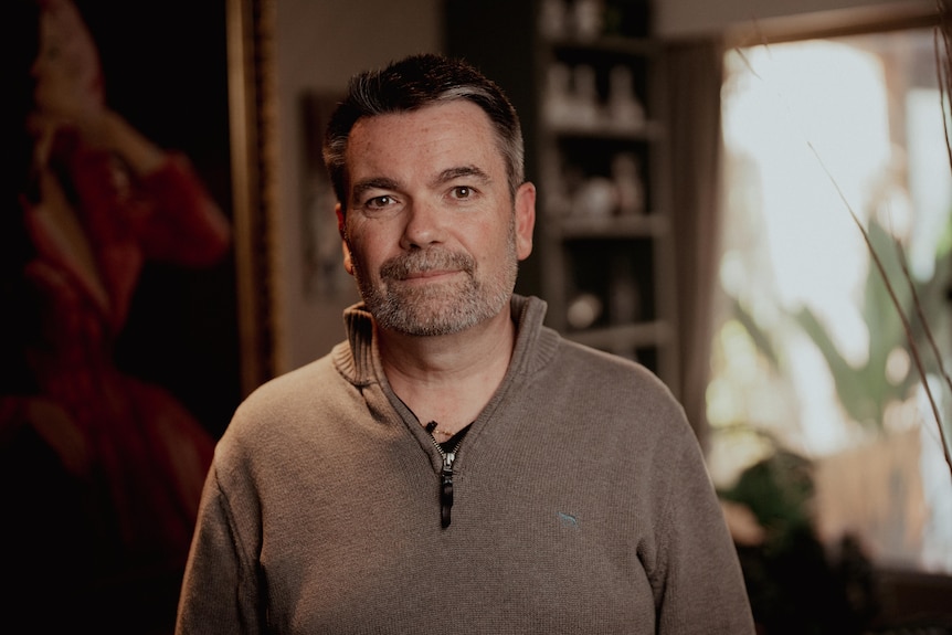 A man in a dark green jumper standing inside a house.