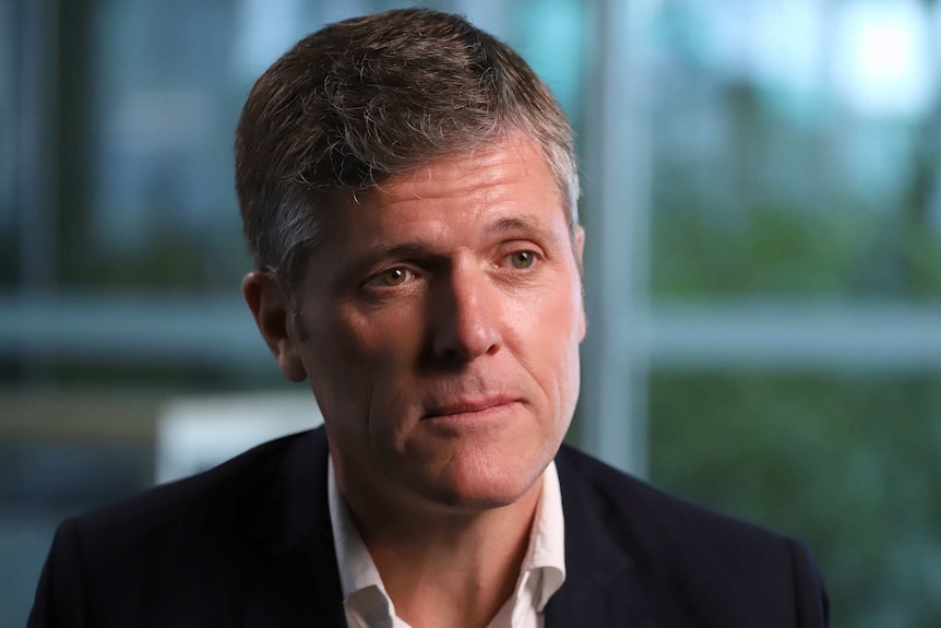 A profile image of a man with short dark and grey hair, wearing a dark suit jacket, looking serious.