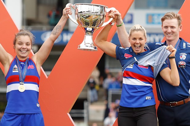 Ellie Blackburn, Katie Brennan and Paul Groves lift the 2018 AFLW premiership cup.