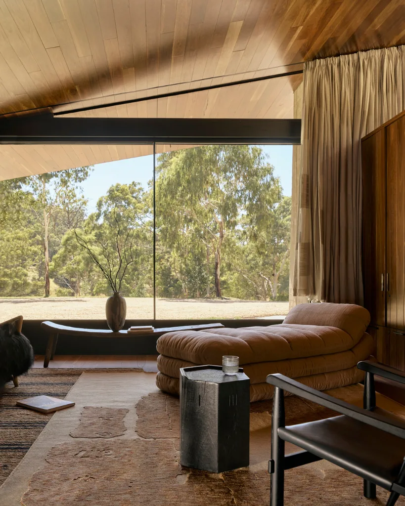 A lounge chaise sits next to windows overlooking the backyard in a modern home