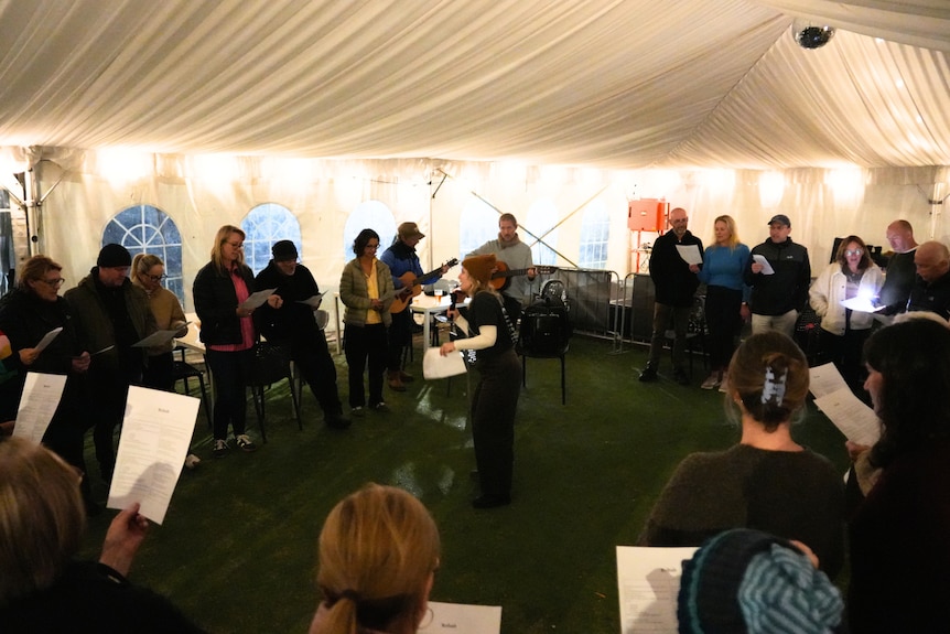 A woman is standing in the middle of a circle, with a microphone in hand as she teaches a group of people to sing.