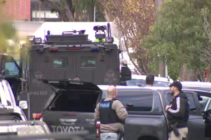 Police and armoured vehicles block suburban street.