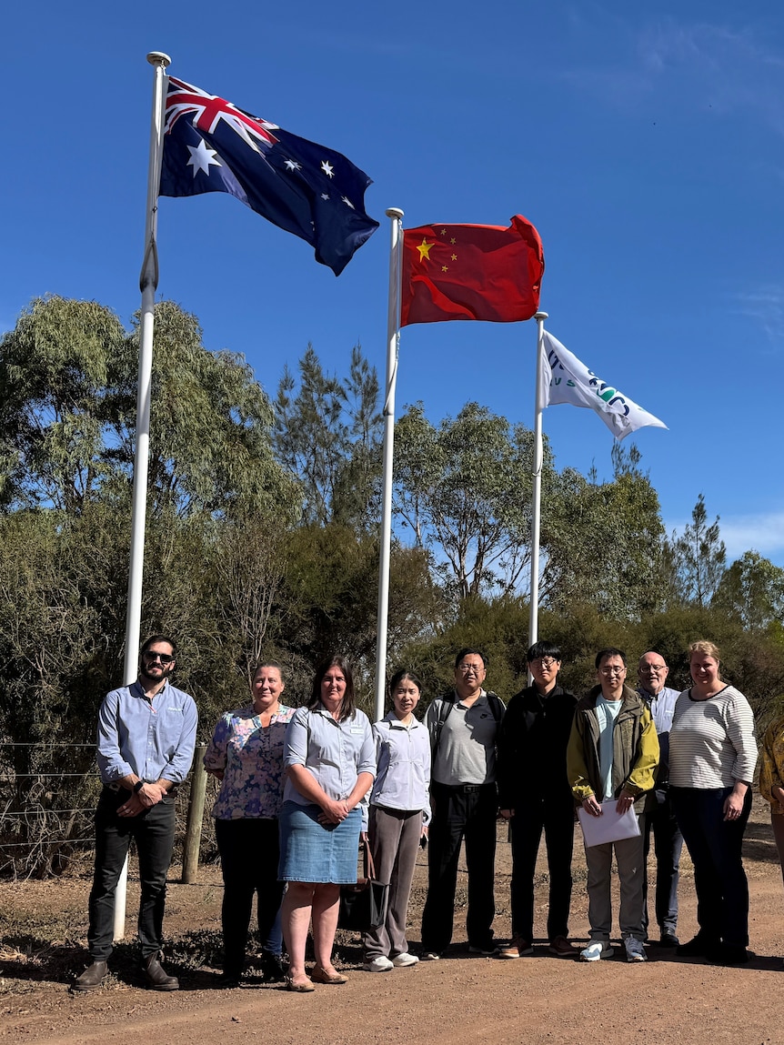 A group of people stand in front of flag poles on a dirt road