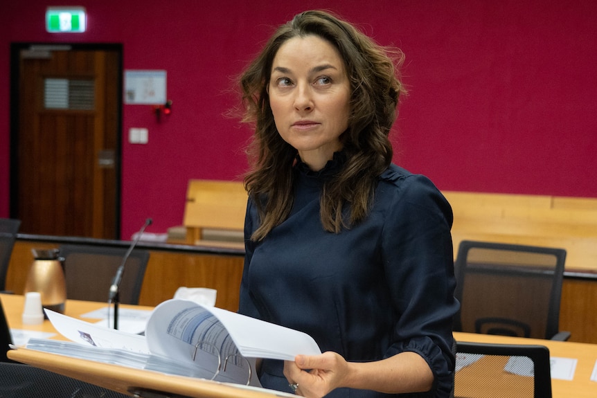 A woman with dark hair leafs through a folder of notes as she sits in a courtroom.
