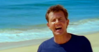 A man sings while walking along a beach.
