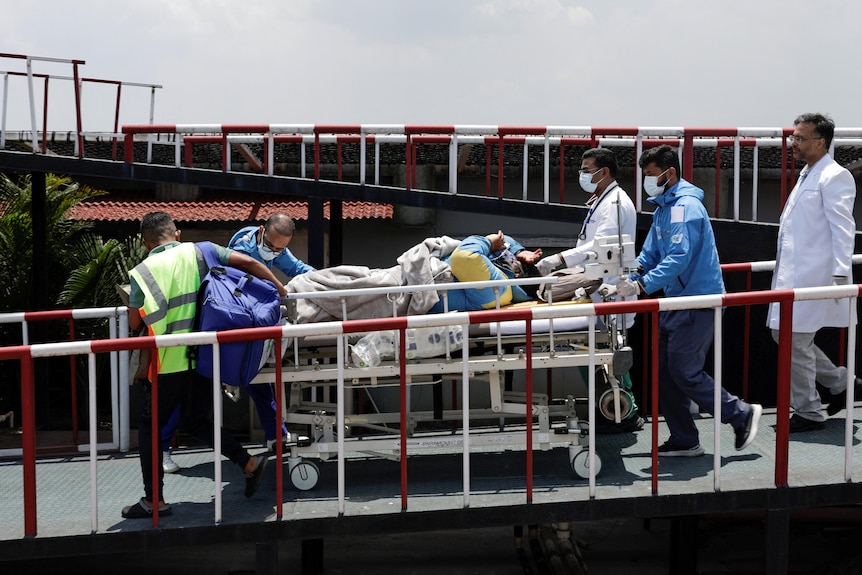 Five paramedics escort a man on a stretcher down a ramp.