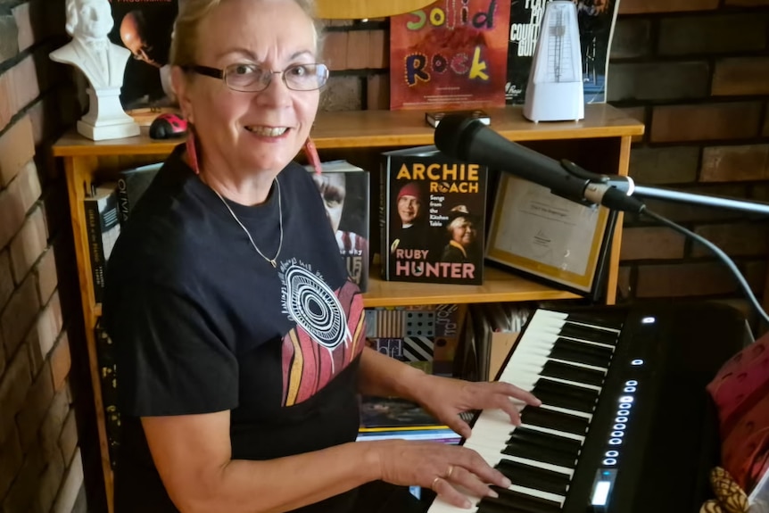 Cheryl sitting at a piano wearing an indigenous t-shirt