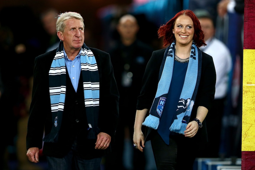 Steve and Erin Mortimer, wearing NSW Blues scarves, walk onto the field before a State of Origin game.