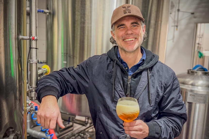 A man holding a beer in front of machinery.