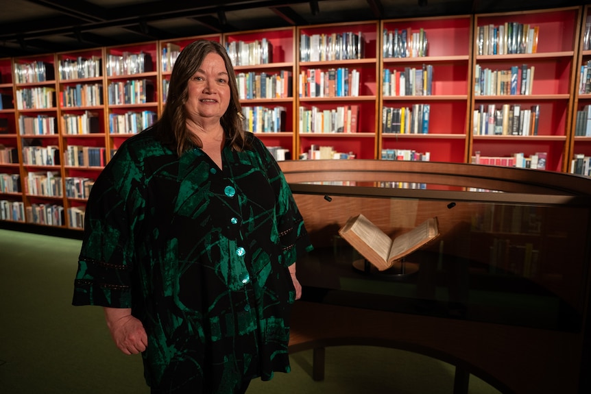 Mary Lijnzaad stands in a library, in front of a copy of Shakespeare's first folio.