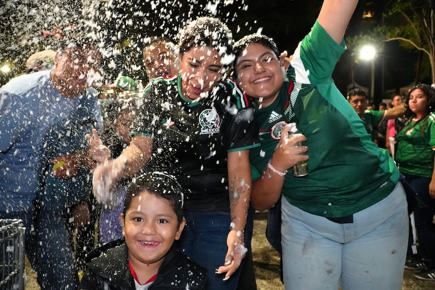 Two women and one young child are sprayed with fake snow as they smile and laugh