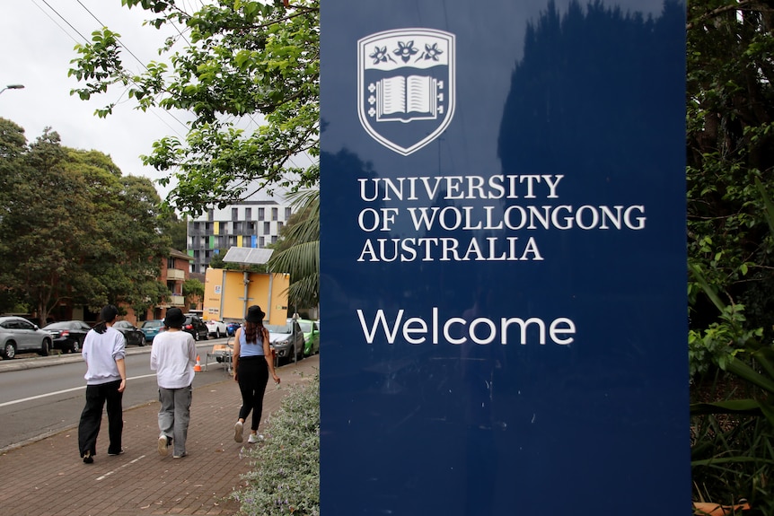 Students walking in carpark, campus sign in foreground