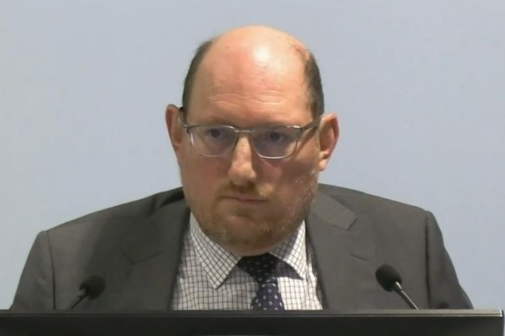 Daniel Rosenfeld in a grey suit and wearing glasses speaking at the commission.
