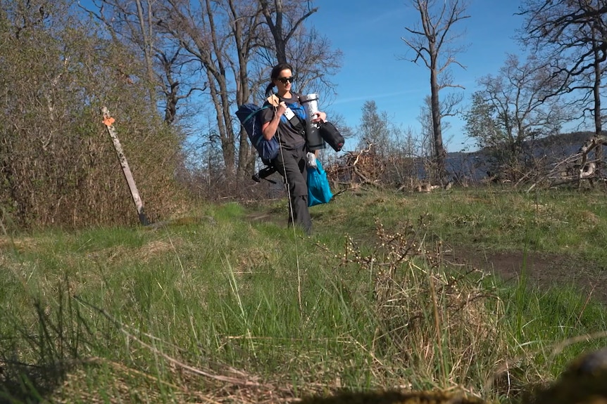 Lucinda carries her camp gear through the woods.
