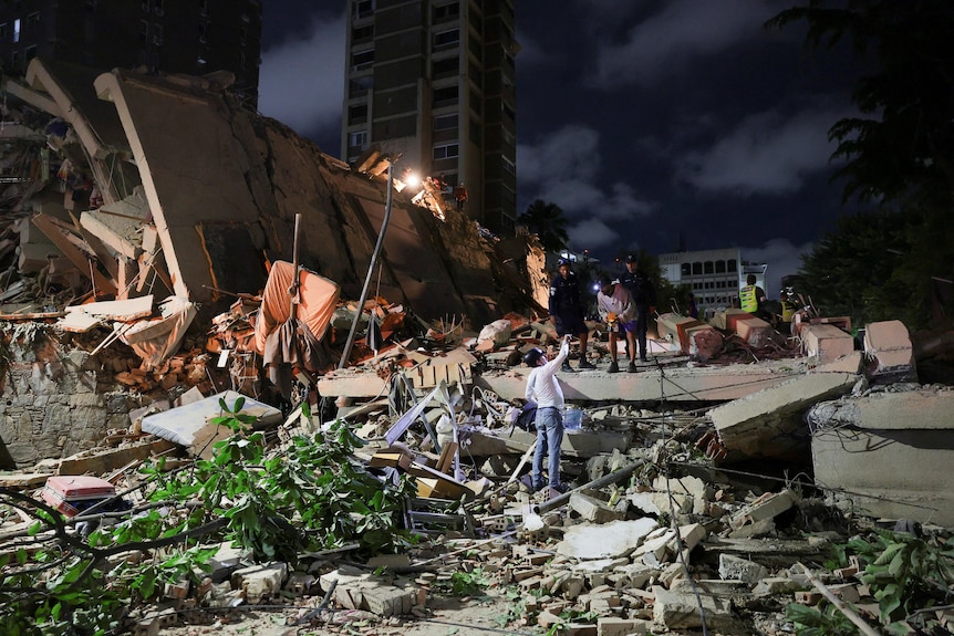 a collapsed building at night - people searching in rubble