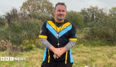 Kevin Rudd, the acting secretary of Elmbridge Eagles Rugby Club. Kevin is standing at the Oaken Lane site and is wearing training gear for the Elmbridge Eagles, including a whistle and grey undershirt.