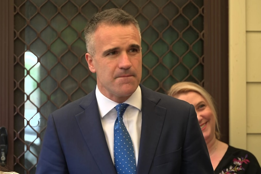 Peter Malinauskas stands in front of a woman outside a house